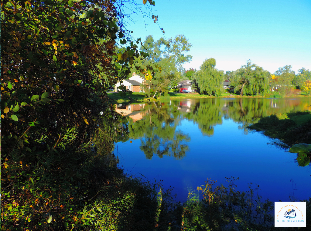 A tranquil lake view in West Bloomfield, MI, reflecting the surrounding homes and trees on the calm water. This area is perfect for buyers looking for lakefront homes in Michigan with peaceful surroundings and natural beauty…