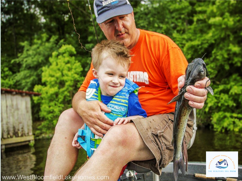 A heartwarming moment of a grandfather and grandson enjoying a day of fishing on a lake in West Bloomfield, MI. The young boy, wearing a life jacket, smiles with excitement as they proudly display their fresh catch. This image captures the joy of lakeside living and the family-friendly atmosphere of West Bloomfield lakefront homes, where residents can enjoy fishing, boating, and quality time by the water…