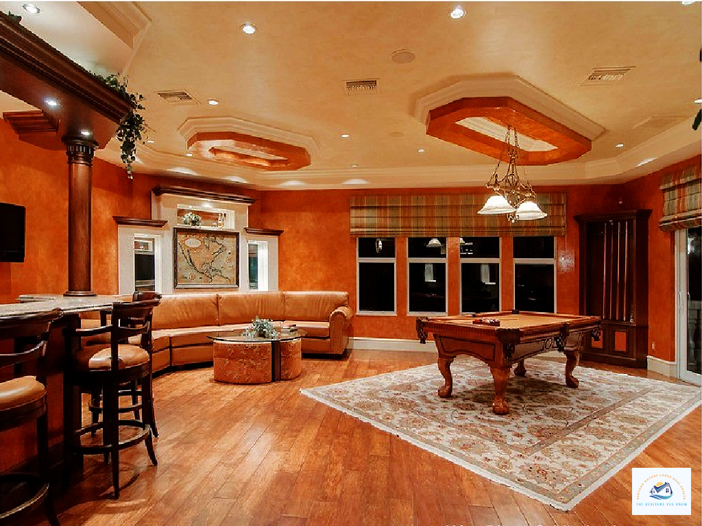 An elegant entertainment room in a luxury lakefront home in West Bloomfield, MI, featuring warm-toned walls, a coffered ceiling, a stylish bar area, and a classic billiards table. This upscale Michigan lake home offers a perfect blend of sophistication and relaxation…